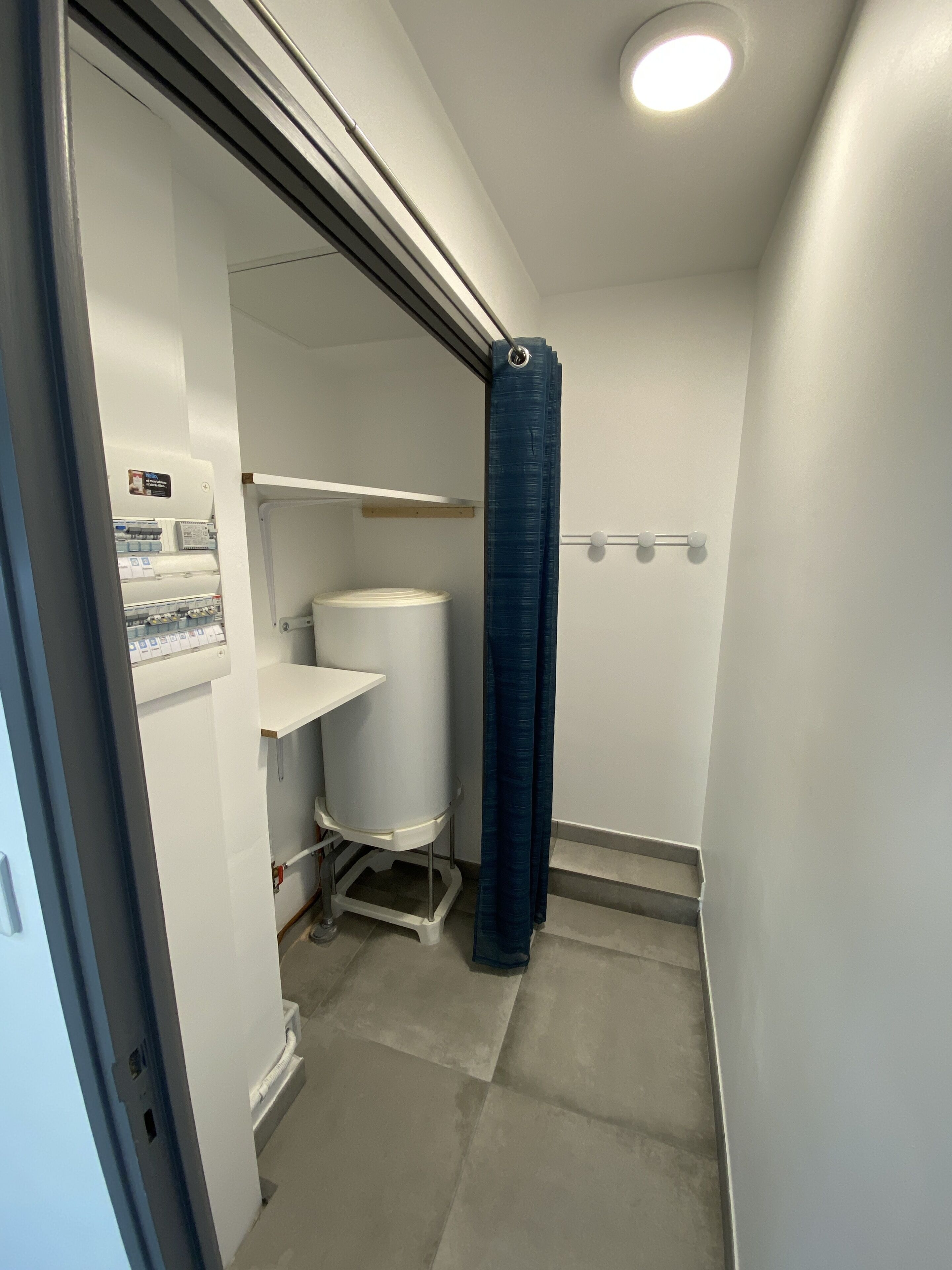 Un baño pequeño y estrecho con inodoro, un estante blanco y una cortina de ducha azul.