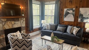 A cozy living room with a stone fireplace, a dark grey sofa with patterned cushions, and a chevron-patterned armchair.
