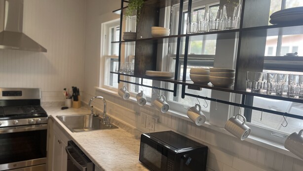 A modern kitchen with stainless steel appliances, a marble countertop, and a black shelving unit with glassware and dishes.