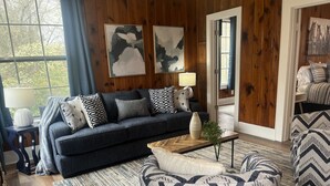 A cozy living room with a dark blue sofa, patterned cushions, a wooden coffee table, and a chevron-patterned armchair.