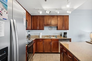 A kitchen with wooden cabinets, a stainless steel refrigerator, a sink, and a coffee maker. - Gulf Views! Updated Resort Condo! Steps 2 Beach (Panama City Beach)