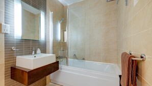 A modern bathroom with a white bathtub, a glass-enclosed shower, and a wooden vanity with a sink.