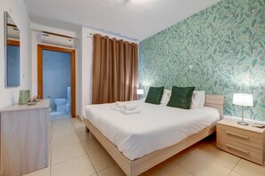Une chambre d’hôtel avec un lit, une table de chevet, une lampe et une salle de bain visible à travers une porte ouverte.