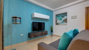A modern living room with a flat-screen TV mounted on a wall, a built-in entertainment unit below it, a floor lamp, and a painting on the wall.