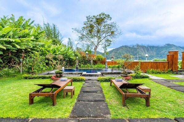 A garden with a stone pathway leading to a pool, surrounded by lush greenery and wooden furniture.