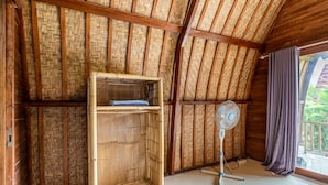 A room with a bamboo wall, a wooden shelf, a standing fan, and a window with curtains. - KINTAMANI Paradise 4BR (Kintamani)