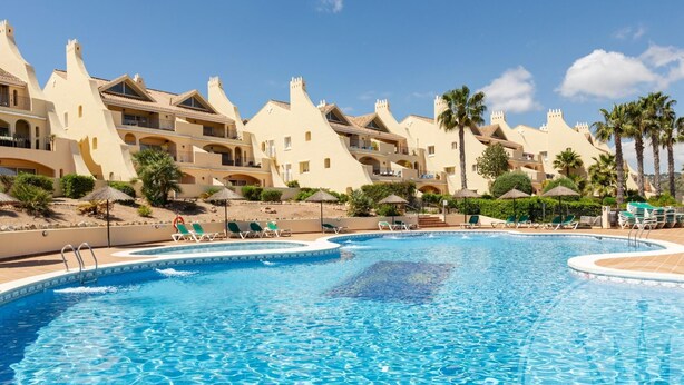 A swimming pool with lounge chairs and a resort building with multiple balconies.