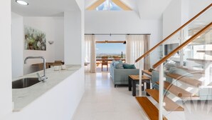 A modern living space with a kitchen, dining area, and a staircase leading to a balcony with a city view.