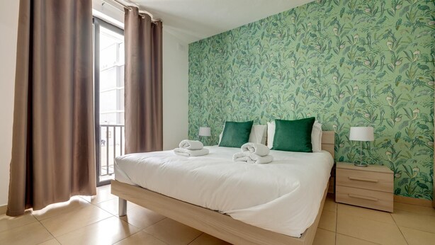 A hotel room with a bed, two pillows, a nightstand, a lamp, and a window with curtains.