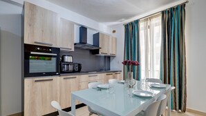 A modern kitchen with a built-in oven, microwave, and coffee maker, a dining table with chairs, and a window with striped curtains.