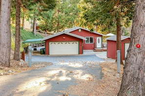 A red cabin with a garage, surrounded by trees and a gravel driveway.