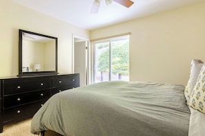 A bedroom with a bed, a dresser, a mirror, and a door leading to a balcony.
