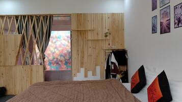 A bedroom with a large bed, wooden panel walls, a wardrobe, and a window with a colorful view.