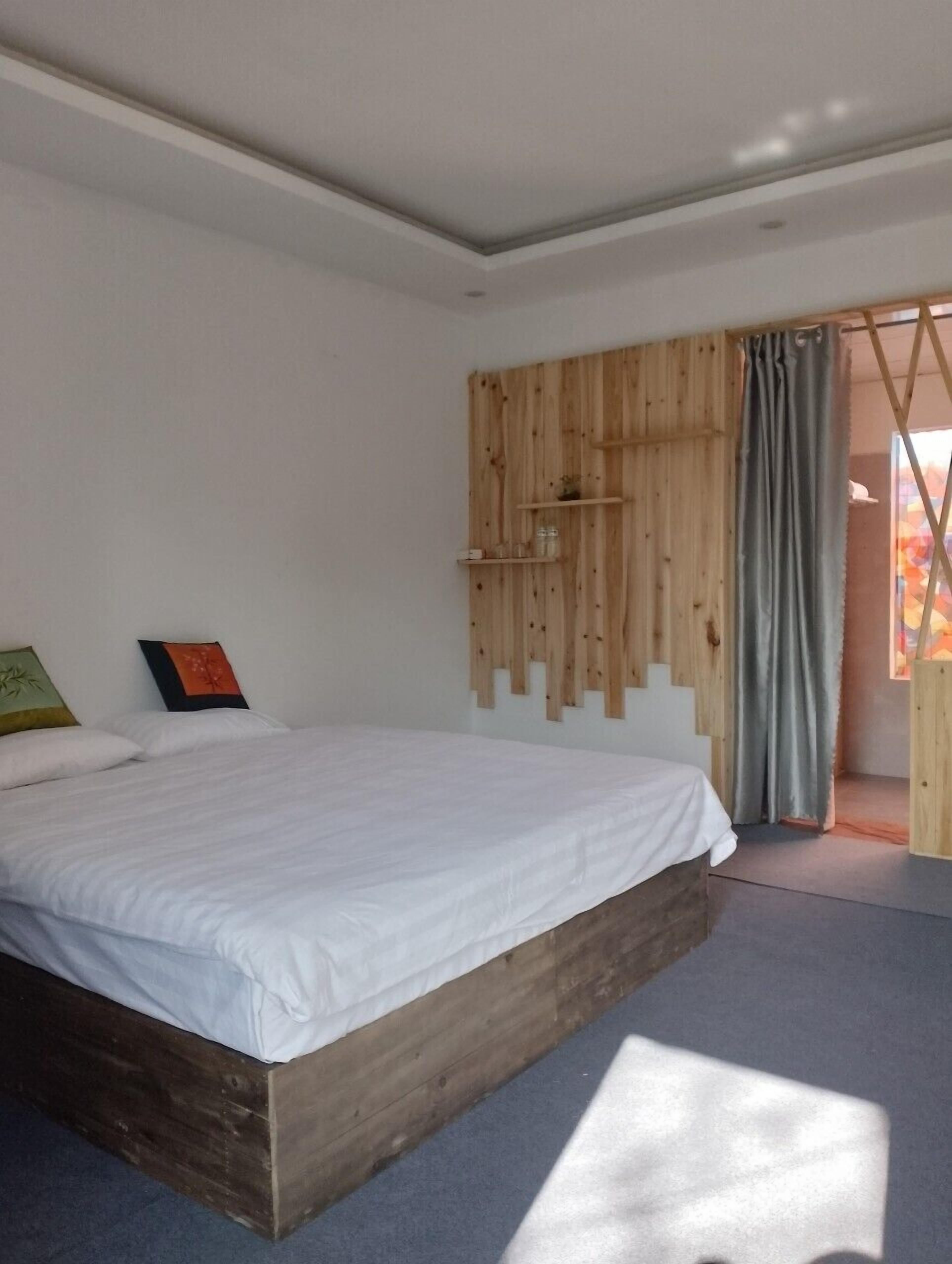 A bedroom with a wooden bed frame, white bedding, a wooden panel wall, and a grey curtain.