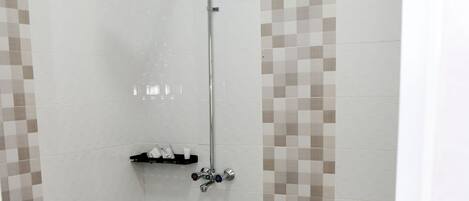 A bathroom with a shower, toilet, and a small shelf with toiletries.