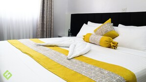 Un lit bien fait, recouvert d’une couverture blanche et jaune, avec deux oreillers et une serviette pliée.
