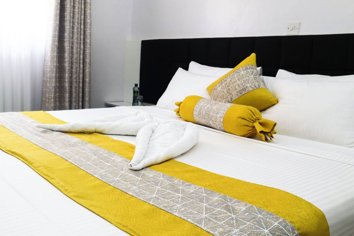 A neatly made bed with a white and yellow bedspread, two pillows, and a folded towel.