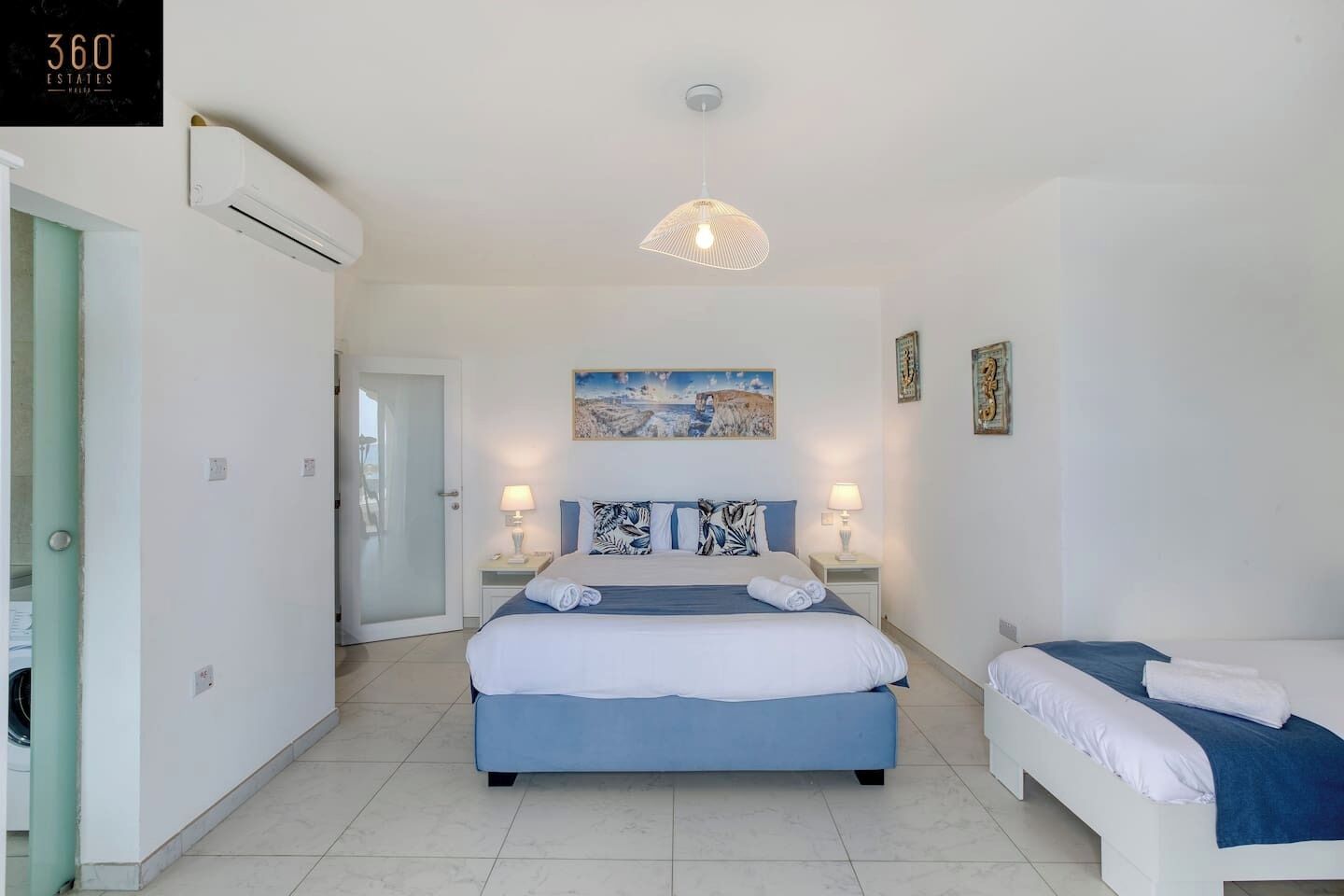 A hotel room with a large bed, two bedside tables with lamps, a painting on the wall, and a door leading to another room.