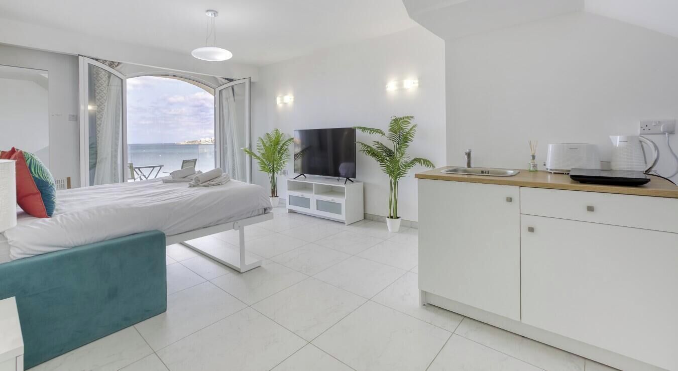 Ein modernes Hotelzimmer mit Bett, Fernseher, einer kleinen Küchenzeile und Meerblick.