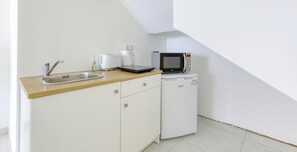 Una kitchenette compacta con un lavamanos, cafetera, microondas y un refrigerador pequeño.