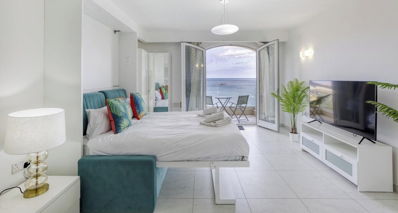 Une chambre d’hôtel moderne équipée d’un lit, d’une télévision, d’un balcon avec vue sur la mer et d’une plante.