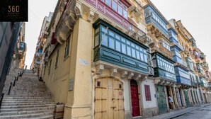 A multi-story building with a staircase leading to the entrance, featuring traditional architectural elements and a variety of colored doors and windows. - Mesmerising Views for a 2BR APT in the Capital ! (Valletta)