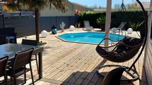 En träaltan med en pool, utomhusmöbler och en hängstol.
