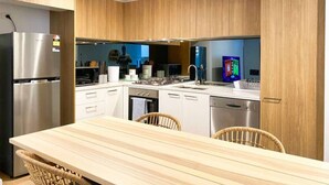Eine moderne Küche mit Holzschränken, Edelstahlgeräten, einem Holzesstisch und einem Fernseher.