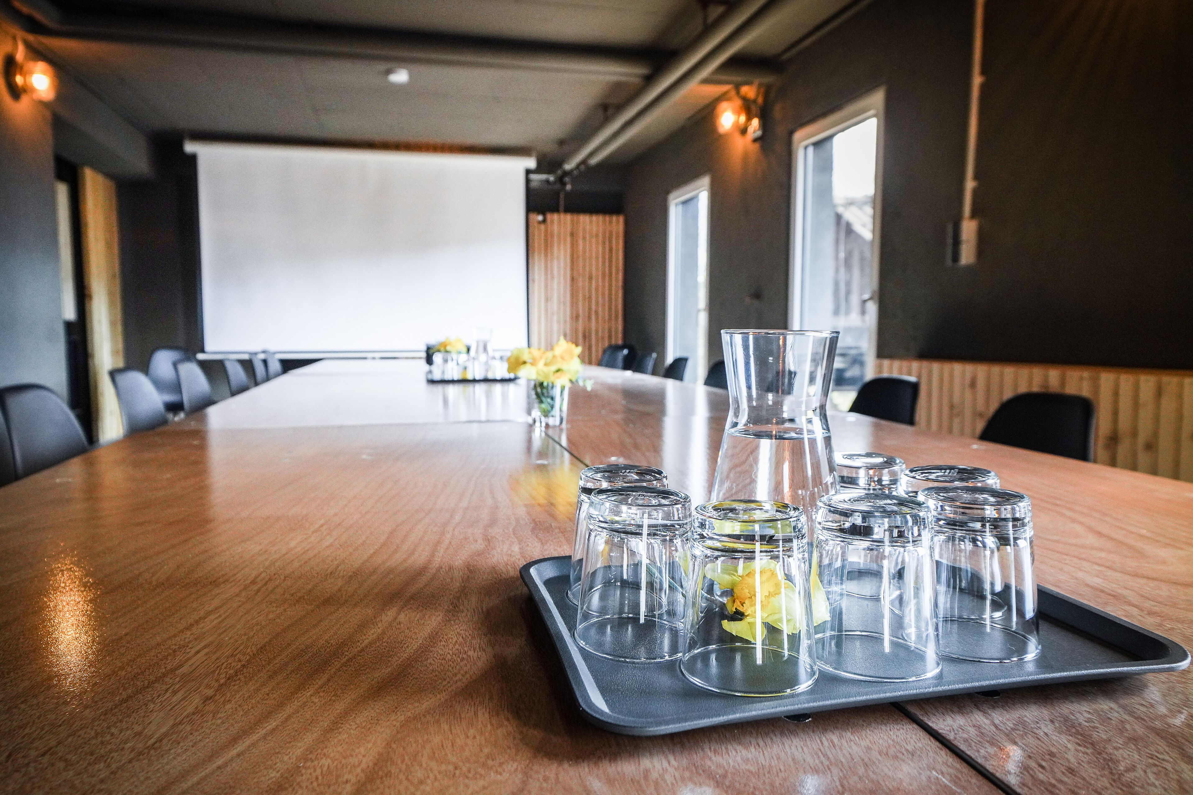 A conference room with a long table, a projector screen, and a tray with glasses and a pitcher.