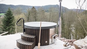 Un bain à remous avec des marches en bois et une cheminée, entouré d’arbres et offrant une vue sur la montagne.