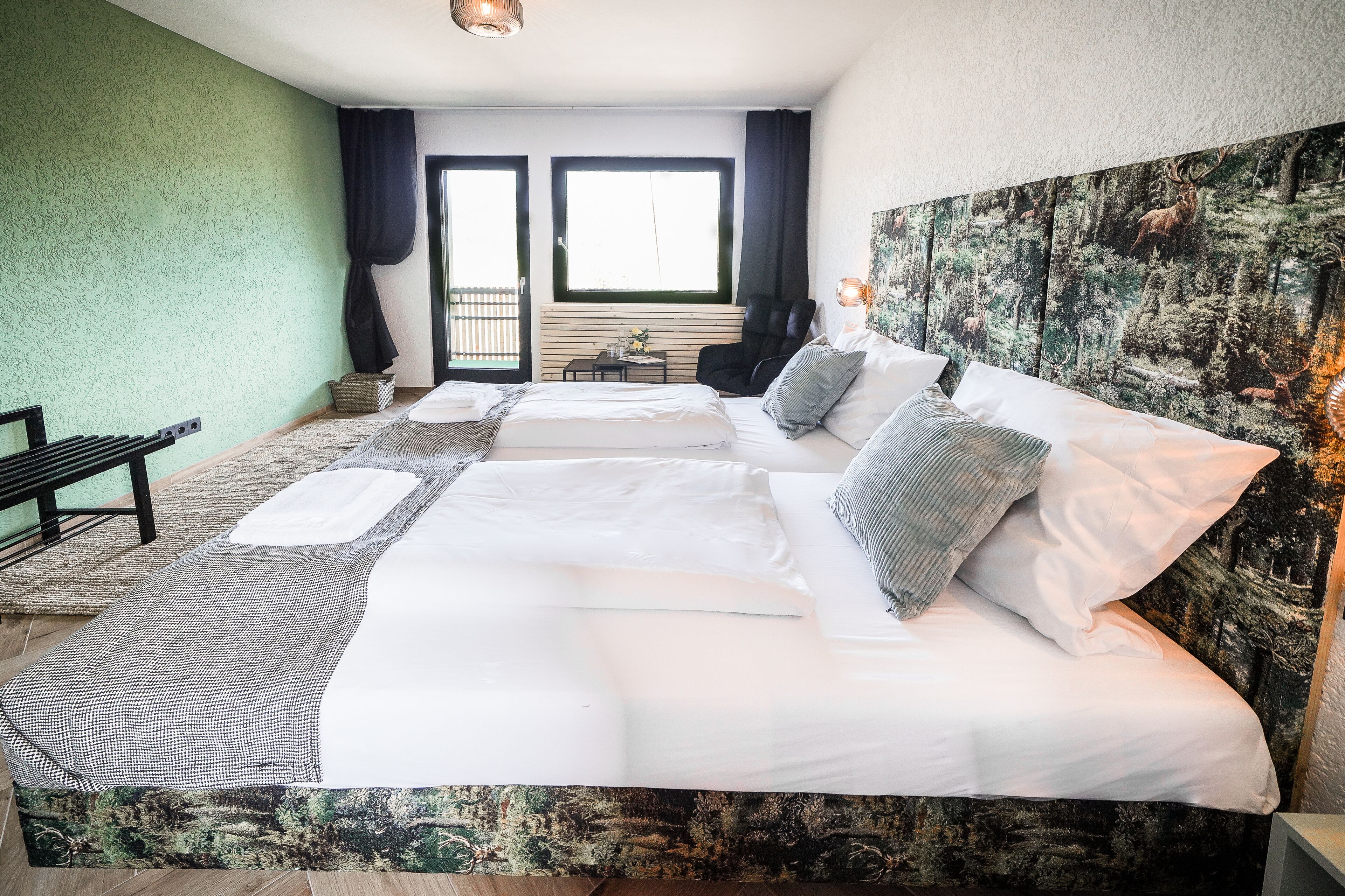Ein großes Bett mit weißen Laken, einem gemusterten Teppich und einem Wandbehang mit Waldmotiv.