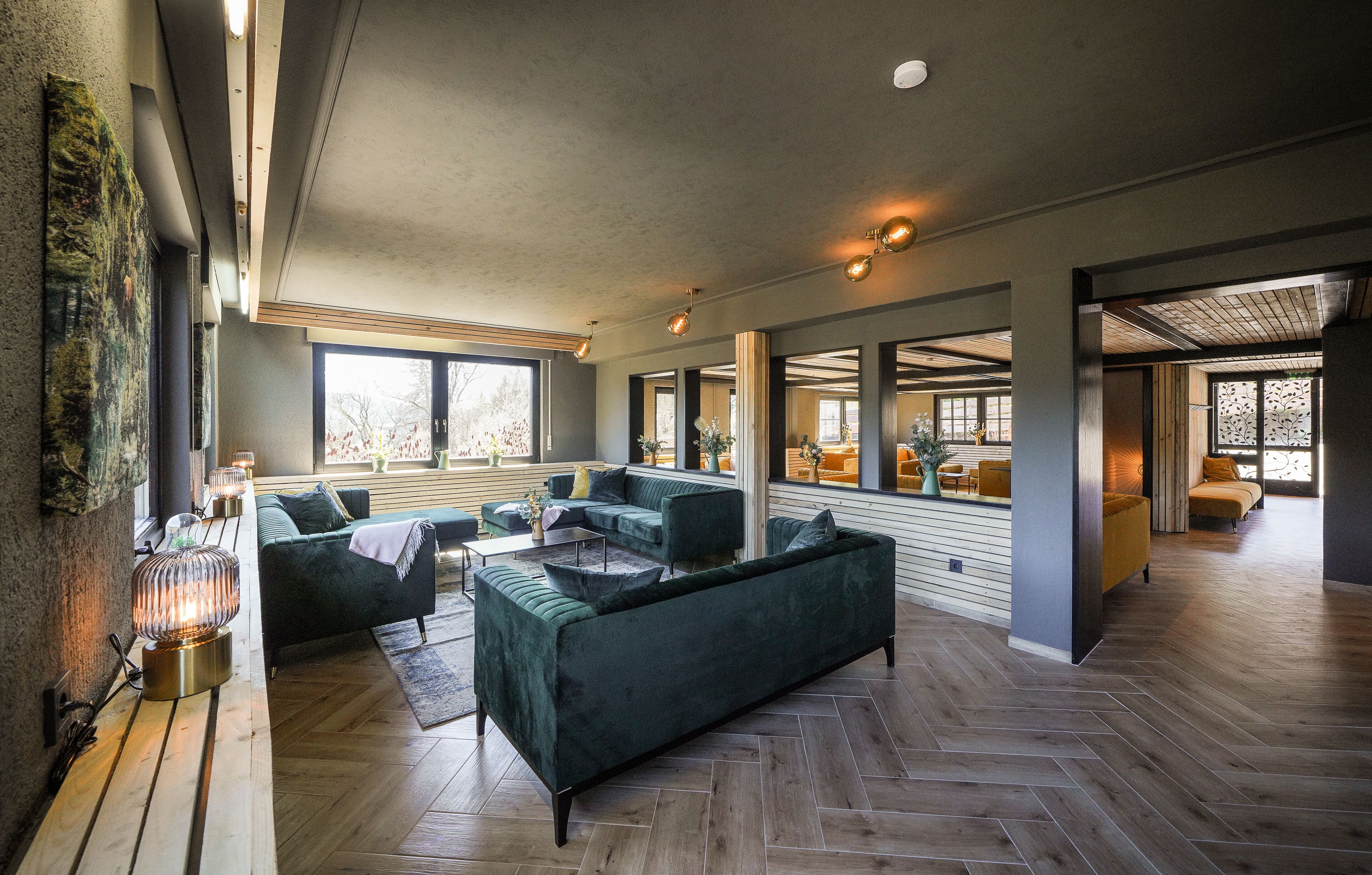 A spacious living area with a large sofa, a coffee table, and a fireplace. There are multiple windows providing natural light and a view of the outside.