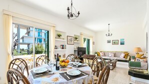 A dining area with a table set for four, surrounded by wicker chairs, a sofa, and a TV.