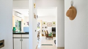 A kitchen with white cabinets, a microwave, and a green vase. There is a dining area with a chair and a TV.