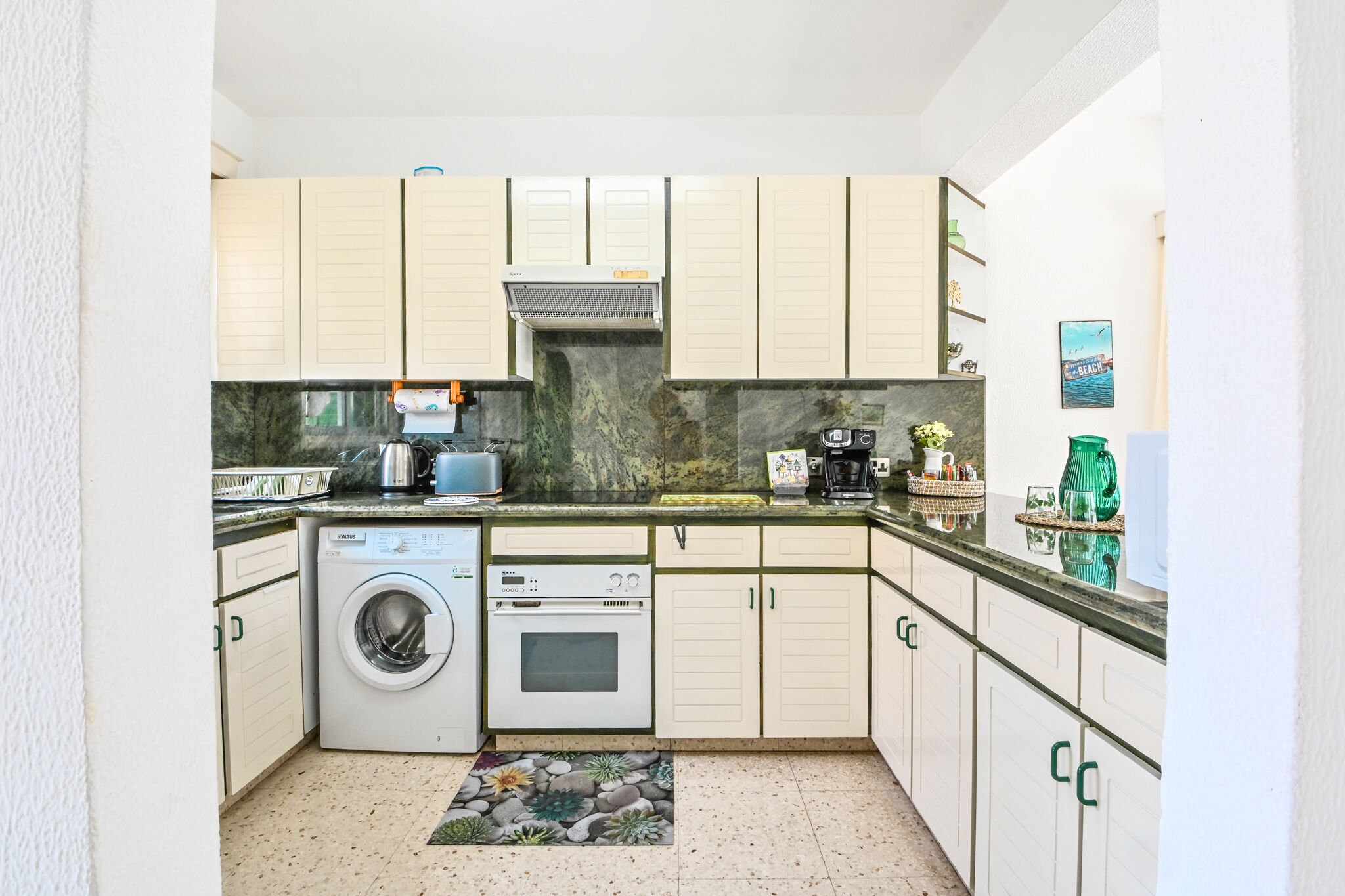 A compact kitchen with a washing machine, oven, and a coffee maker.