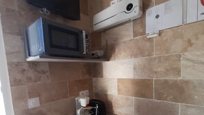 Uma cozinha compacta com micro-ondas, máquina de café e torradeira em uma bancada.