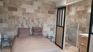 Quarto moderno com cama grande, cabeceira decorativa, closet espaçoso e área de chuveiro.