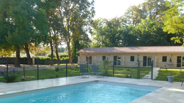Piscina com deck ladrilhado, cercada por uma cerca e árvores.