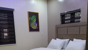 Un dormitorio con cama, cabecera, ventana con persianas y una obra de arte colgada en la pared.