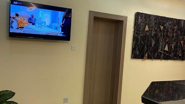 Una habitación con una televisión montada en la pared, una puerta de madera y una obra de arte abstracta.