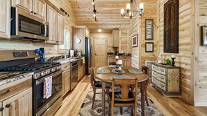 A wooden interior with a kitchen area featuring a stove, microwave, and cabinets. There is a dining table with chairs and a chandelier.