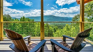 A wooden deck with two Adirondack chairs facing a scenic mountain view.