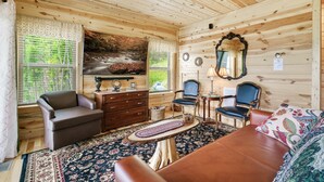 A wooden cabin interior with a sofa, chairs, a dresser, and a painting of a waterfall.