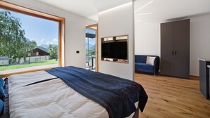 A modern bedroom with a large bed, a TV, a wardrobe, and a view of the outdoors.