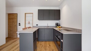 A modern kitchen with grey cabinets, a wooden door, and a marble countertop.