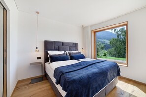 Ein Schlafzimmer mit großem Fenster, einem Bett mit dunklem Kopfteil und einem Nachttisch mit Lampe.