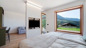 A bedroom with a bed, a TV mounted on the wall, and a large window with a view of a house and mountains. - Studio 'Alivo Living Apartment Olivia' with Mountain View, Shared Terrace and Wi-Fi (Riffian)
