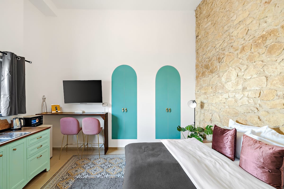 Ein Schlafzimmer mit einem Bett, einem Schreibtisch mit Computer, zwei Stühlen, einem Fernseher und einer Steinwand.