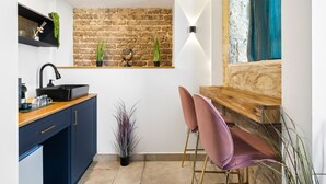 A modern kitchen with a brick wall, wooden countertop, and two pink chairs. - Helios Boutique Suites by La Finca Hotel (Beersheba)