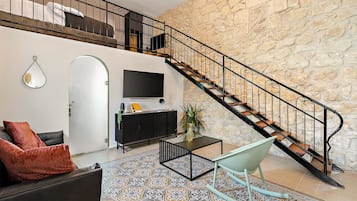 Een moderne woonkamer met een stenen muur, een zwarte bank, een salontafel en een trap met een metalen leuning.